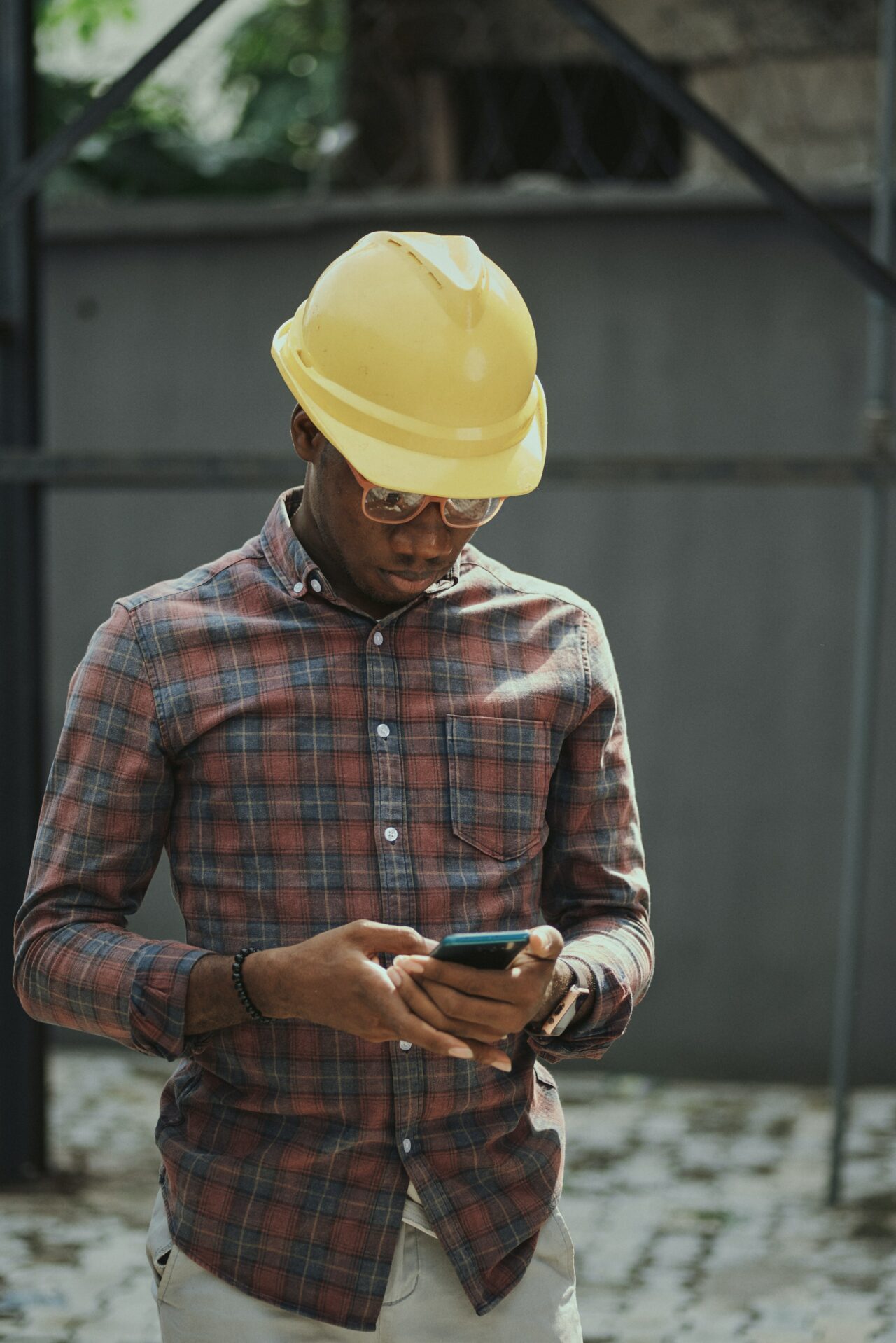 Mann auf einer Baustelle mit Helm schaut auf sein Smartphone