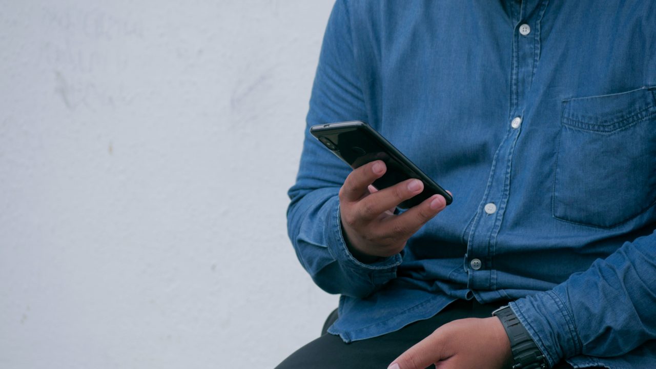 Mann mit blauen Hemd und Smartphone in der Hand