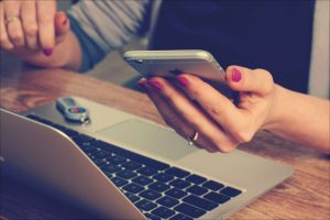 Frau sitzt vor ihrem Laptop mit einem Mobiltelefon in der Hand