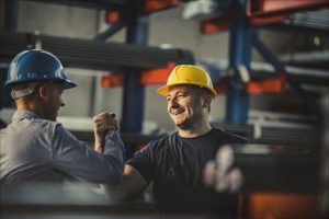 two men with safety helmets holding hands in high bay warehouse