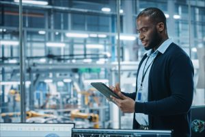 Man in shirt holding tablet and in background you can see production