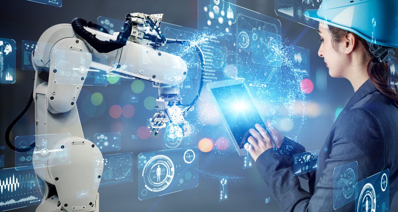 women with helmet and a tablet in her hands looks at a roboter arm